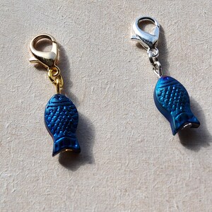 May include: Two blue fish charms with gold and silver lobster clasps. The charms are iridescent and have a textured surface.