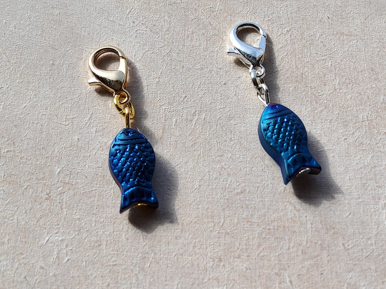 May include: Two blue fish charms with gold and silver lobster clasps. The charms are iridescent and have a textured surface.