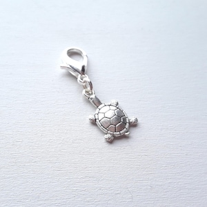 Op de afbeelding: Een zilverkleurige schildpadbedel met een karabijnsluiting. De schildpad heeft een gedetailleerd schildpatroon en kleine, afgeronde voetjes. De bedel is ontworpen om aan een armband of ketting te worden bevestigd.