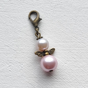 Op de afbeelding: Een vintage-stijl bedel met een parel engel hanger. De bedel heeft een bronskleurige sluiting en verbindingsstukken. De engel hanger heeft twee parels, een lichtroze en een gebroken witte, met bronskleurige vleugels.