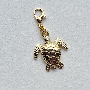 May include: A gold-coloured turtle charm with a lobster clasp. The turtle has detailed shell and flipper designs. Suitable for jewellery making or as a decorative accent.