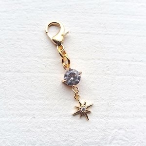 Può includere: Un charm dorato con chiusura a moschettone, una gemma grigia rotonda centrale e un ciondolo a forma di stella. Ideale per la creazione di gioielli o come accessorio.