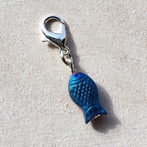 May include: A silver charm with a blue fish design. The fish has a textured surface and a silver loop for attaching to a chain or bracelet.