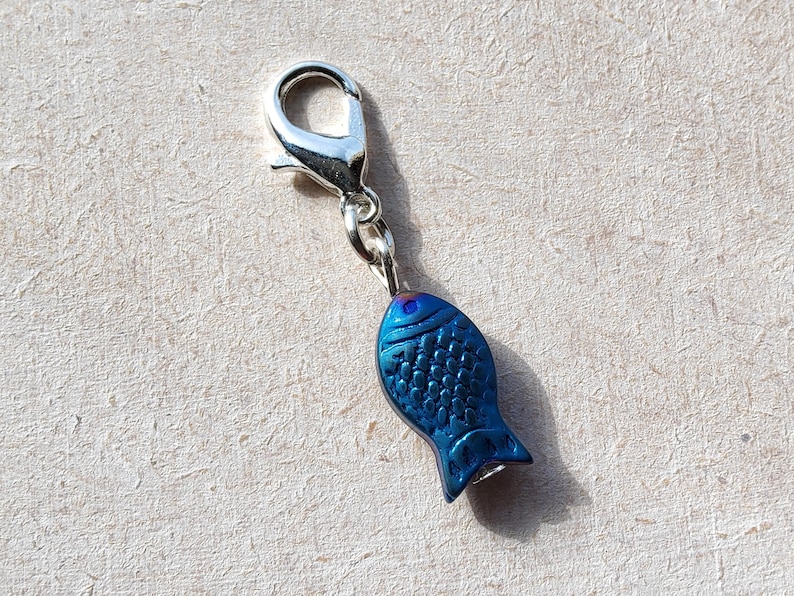 May include: A silver charm with a blue fish design. The fish has a textured surface and a silver loop for attaching to a chain or bracelet.