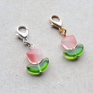 May include: Two pink and green tulip-shaped charms with silver and gold clasps. The charms are made of glass and have a delicate, feminine design.