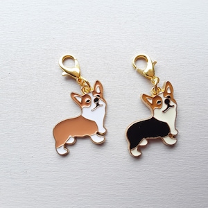 Peut inclure: Deux breloques en métal couleur or en forme de corgis. Un corgi est brun, blanc et noir. L'autre corgi est noir, blanc et brun. Les deux breloques ont une boucle en métal couleur or.