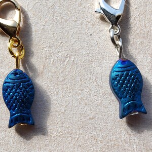 May include: Two blue fish charms with gold and silver lobster clasps. The fish charms have a textured surface and are a dark blue color.