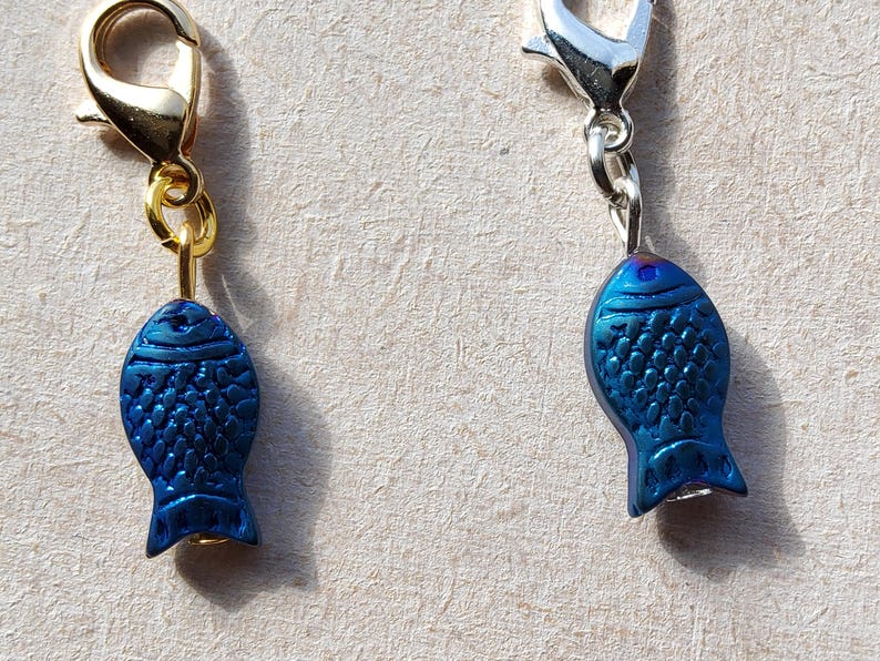 May include: Two blue fish charms with gold and silver lobster clasps. The fish charms have a textured surface and are a dark blue color.
