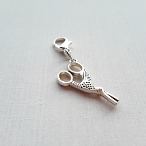 Puede incluir: Encanto de plata en forma de tijeras con un diseño decorativo. El encanto tiene un cierre de langosta para sujetarlo a una pulsera o collar.