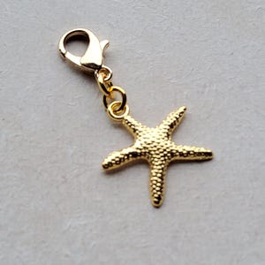 Könnte beinhalten: Goldfarbener Seestern-Anhänger mit einem Karabinerverschluss. Der Anhänger ist etwa 3,8 cm breit.