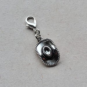 May include: Silver charm with a cowboy hat design. The charm has a silver loop for attaching to a bracelet or necklace.