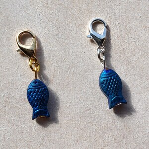 May include: Two blue fish charms with gold and silver lobster clasps. The charms are a popular addition to jewelry, bags, and keychains.