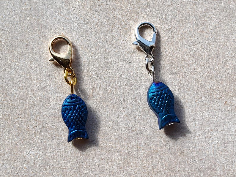 May include: Two blue fish charms with gold and silver lobster clasps. The charms are a popular addition to jewelry, bags, and keychains.