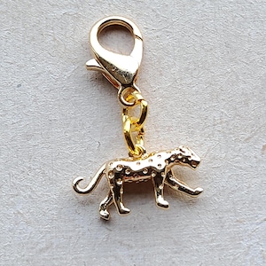 May include: A gold-coloured charm featuring a leopard design. The charm is attached to a lobster clasp, allowing it to be easily added to a bracelet or necklace. The leopard has a spotted pattern and is in a walking pose.