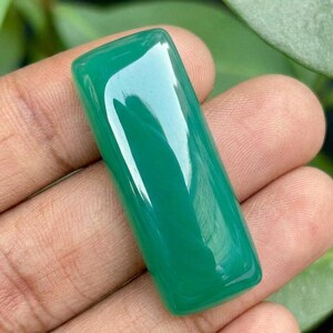 May include: A smooth, rectangular cabochon gemstone with a vibrant, solid green color and a polished, reflective surface. The stone features rounded corners and a flat base, showcasing a consistent, opaque emerald-green hue throughout its entire body.