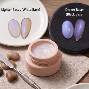 May include: A close-up of nail art supplies. The image shows two sets of nail tips, one on a white plate and the other on a black plate. A small jar of iridescent gel and a metal spatula are also visible. The text "Lighter Bases (White Base)" and "Darker Bases (Black Base)" are present.