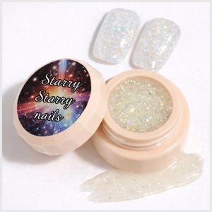 May include: A round, light peach-coloured jar of iridescent nail glitter with a lid featuring a galaxy print and the text Starry Starry nails. Two clear, glitter-coated nail tips are positioned above the open jar with a smear of gel.