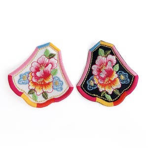 May include: Two embroidered floral patches. One has a white background, a pink border, and a colourful flower. The other has a black background, a pink border, and a colourful flower. Both patches have a fan-like shape.