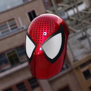 Puede incluir: Una máscara roja brillante de Spider-Man con lentes oculares blancas y ribetes negros. La máscara tiene un diseño perforado en la parte superior y en la zona de la boca. El fondo está borroso, mostrando un edificio.
