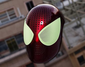 May include: A glossy, burgundy-colored helmet with a design reminiscent of a superhero mask. The helmet features light green eye coverings and numerous small perforations across the surface. The design is set against a blurred urban background.
