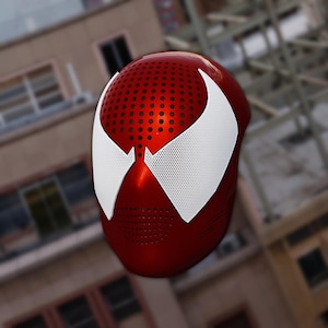 Könnte beinhalten: Ein metallisch roter Integralhelm mit einer glatten, abgerundeten Oberfläche und einer perforierten Textur im Stirn- und Kinnbereich. Große, weiße, dreieckige Augenlinsen mit einem feinen Netzmuster befinden sich auf der Vorderseite.