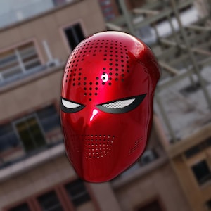 May include: A glossy red full-face mask with a perforated top and mouth area. The mask features white eye slits with a black mesh backing. The design is reminiscent of a superhero or comic book character.