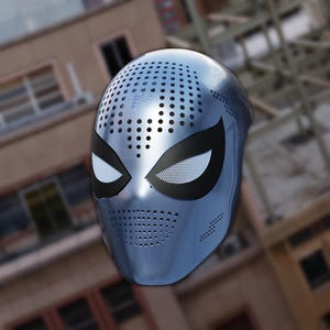 Op de afbeelding: Een metallic blauw superheldenmasker met een geperforeerd ontwerp. Het masker heeft zwarte oogbedekkingen met wit gaas en een reeks kleine gaatjes over het gezicht. Een spinnenembleem is zichtbaar op het voorhoofd.