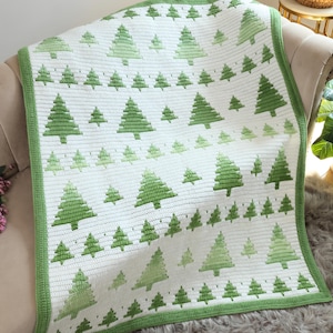 May include: A white crochet blanket featuring a repeating pattern of green pine trees in varying sizes. The blanket is finished with a solid green border and displays rows of small and large trees across the entire rectangular surface.