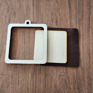 May include: A wooden square frame with a cutout for a picture or embroidery. The frame is attached to a brown felt backing.