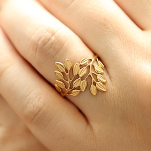 Könnte beinhalten: Ein goldfarbener Ring mit einem Blattdesign. Der Ring wird an einem Finger getragen und hat ein filigranes, durchbrochenes Muster aus Blättern. Der Ring besteht aus einem glänzenden, metallischen Material.