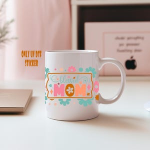 A white mug with a colorful design featuring the text "blessed mom" and various floral and geometric patterns.