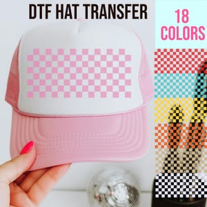 May include: Pink trucker hat with a white front panel featuring a pink and white checkered design. The text "DTF HAT TRANSFER" is at the top, and "18 COLORS" is on the right, with color swatches.