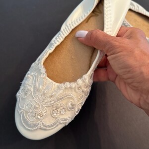 Puede incluir: Una bailarina blanca con punta redondeada y suela interior color canela. El exterior est&aacute; adornado con bordados de encaje floral blanco, lentejuelas transparentes y peque&ntilde;as cuentas blancas en la puntera. El zapato tiene un borde el&aacute;stico.