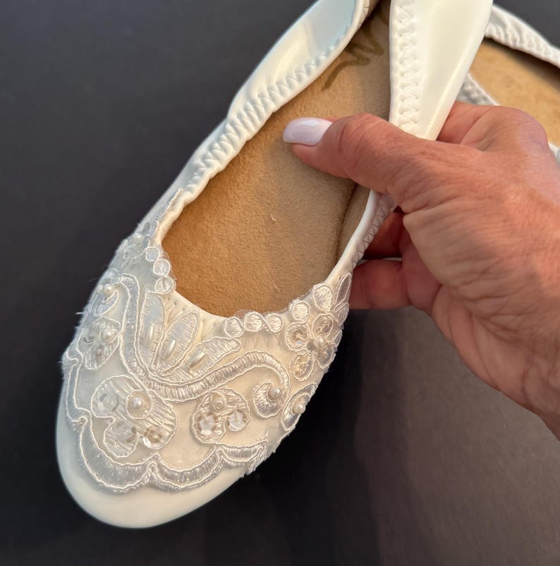 Puede incluir: Una bailarina blanca con punta redondeada y suela interior color canela. El exterior est&aacute; adornado con bordados de encaje floral blanco, lentejuelas transparentes y peque&ntilde;as cuentas blancas en la puntera. El zapato tiene un borde el&aacute;stico.