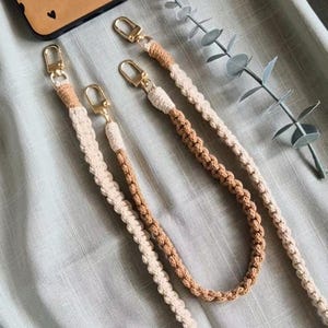 Può includere: Due cordini in macramè realizzati con corda intrecciata nei toni del crema e del marrone chiaro. Ogni cordino è rifinito con chiusure a moschettone in metallo dorato su entrambe le estremità, offrendo un punto di aggancio sicuro.
