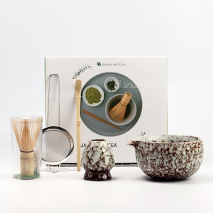 Op de afbeelding: Een matcha theeset met een garde, zeef, lepel en een keramische kom. De set bevat een matcha kom, een chashaku, een chasen en een zeef. De doos op de achtergrond zegt "Green Matcha".