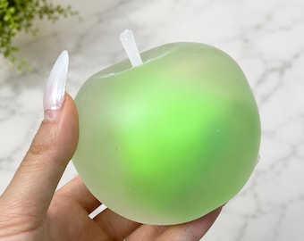 May include: A translucent, light green apple-shaped object with a smooth, matte finish and a small, white, cylindrical stem protruding from the top. The object has a rounded, bulbous form and a soft, semi-opaque appearance throughout its surface.