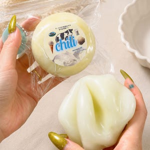 May include: A package of round, light yellow ice cream with the word "chili" on the label. The label also features a cow illustration and ice cream cone. A second, light yellow, flower-shaped ice cream is held in a hand.