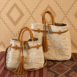 May include: Two woven straw handbags with brown leather accents. The bags have braided handles, leather straps, and decorative tassels. One bag has a shoulder strap. The bags are set against a patterned background.