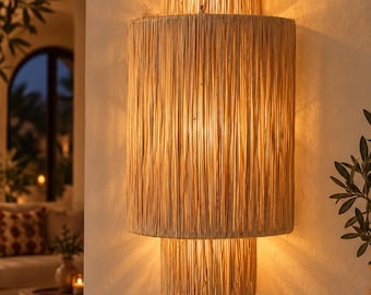 May include: A wall-mounted light fixture featuring a three-tiered cylindrical design constructed from natural tan raffia or straw fibers. The lamp emits a warm, diffused glow from the top and bottom, casting light patterns against the wall surface.