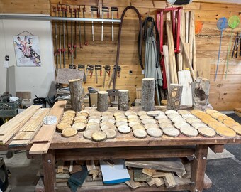 May include: A workshop table displays various woodworking projects. There are numerous wooden coasters, cut from tree branches, alongside several wooden blocks and planks. The scene is set in a rustic workshop with tools and materials.