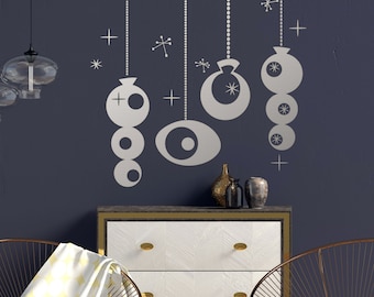 May include: A dark blue wall with a silver Christmas ornament decal. The decal features a series of circles and stars. Two gold chairs and a white dresser with gold accents are in front of the wall.