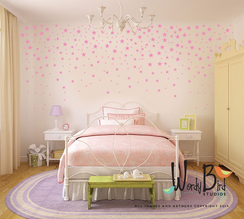 May include: A bedroom scene with a white bed, pink bedding, and a green bench. Pink star decals adorn the white walls. A round purple rug sits on the wooden floor. A chandelier hangs from the ceiling. The room has a soft, inviting atmosphere.