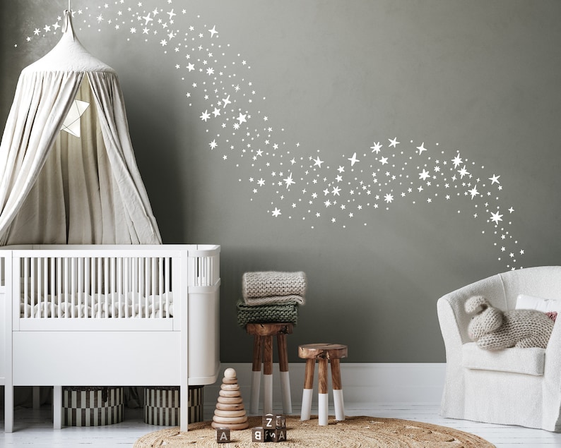 May include: A white cot with a white canopy and a white armchair in a nursery with a grey wall featuring a white star decal design.