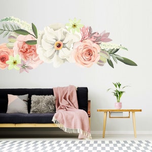 May include: A floral wall decal with pink, white, and green flowers. The decal is placed above a black couch with pink throw blankets and pillows. A small wooden table with a potted plant sits in the foreground.