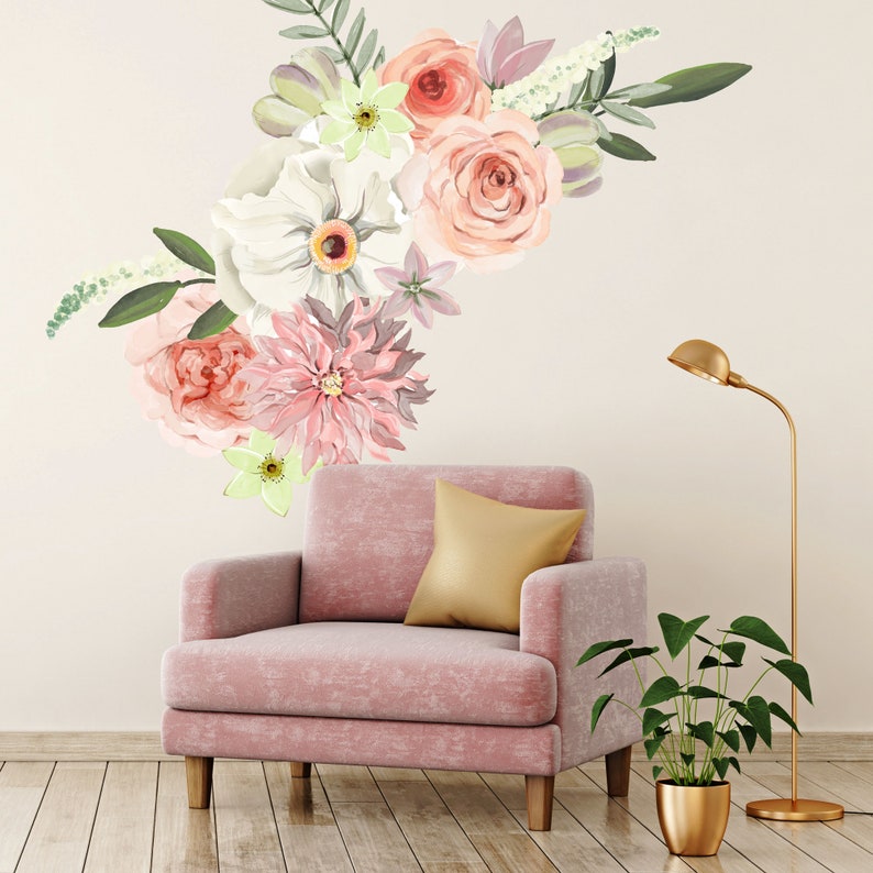 May include: A pink armchair with a gold pillow sits in front of a white wall with a floral decal. The decal features pink, white, and green flowers.