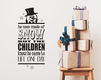 May include: A black and white snowman illustration with the text "he was made of SNOW BUT THE CHILDREN know he came to LIFE ONE DAY". A stack of wrapped gifts with blue and gray ribbon sits on a wooden chair.