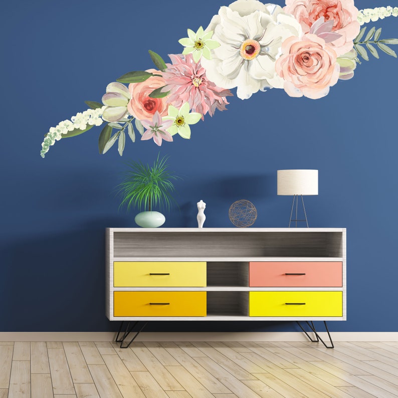 May include: A white dresser with three drawers and two shelves. The drawers are painted yellow and the shelves are white. The dresser is on a wooden floor. A floral wall decal is on the wall behind the dresser.