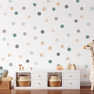 Puede incluir: Una pared blanca decorada con lunares de acuarela en varios colores, incluyendo gris, verde y beige. Un mueble blanco con cestas tejidas y un peluche de jirafa est&aacute;n en primer plano. Un peluche de ballena descansa sobre una cesta de mimbre.