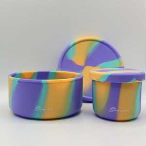 May include: A set of three silicone containers in a swirl pattern of purple, yellow, and teal. The set includes a round bowl, a small lidded container, and a plate. The brand name "Bumble & Ivy" is printed on the bowl and container.